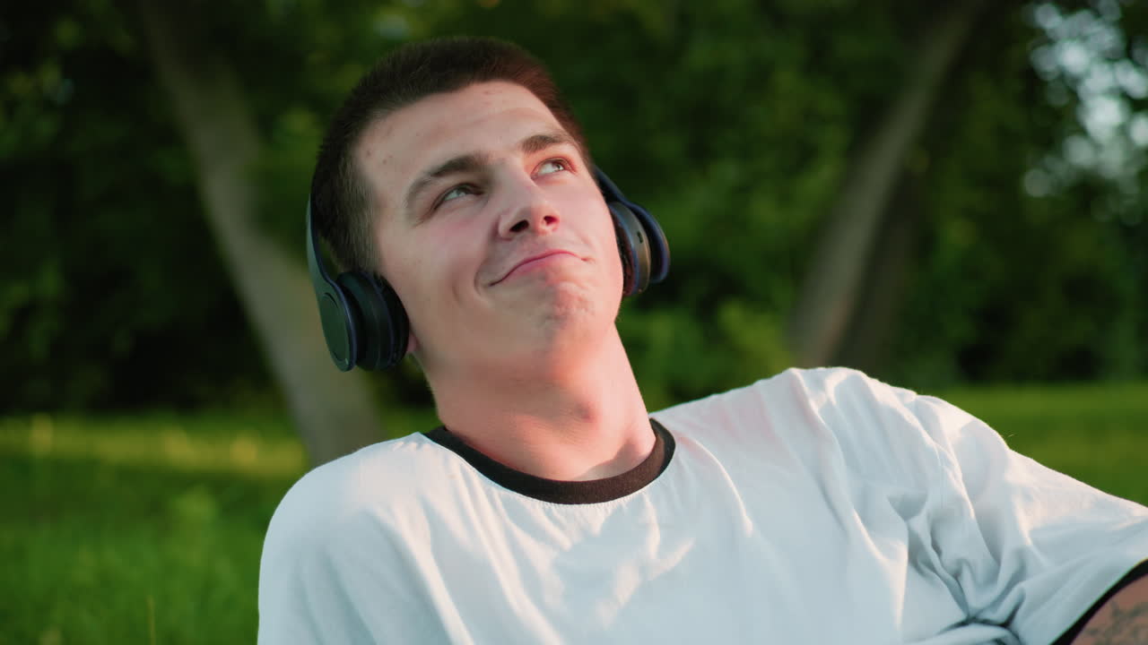 헤드폰을 착용하고 머리를 흔들며 음악을 즐기는 예술가, 미묘한 미소와 문신한 팔, 푸른 야외에 둘러싸여, 평온과 휴식을 반영하고, 진정된 자연 빛으로