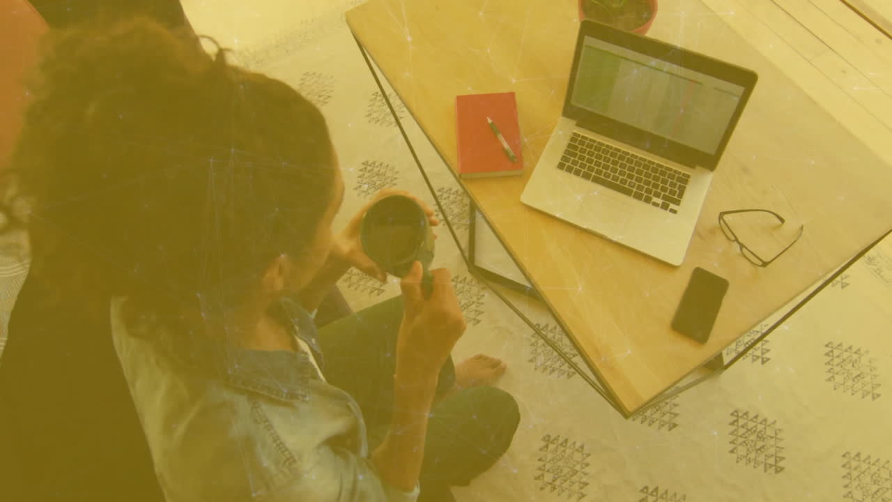 Home-based woman sipping coffee while using laptop, featuring animated finance charts above screen