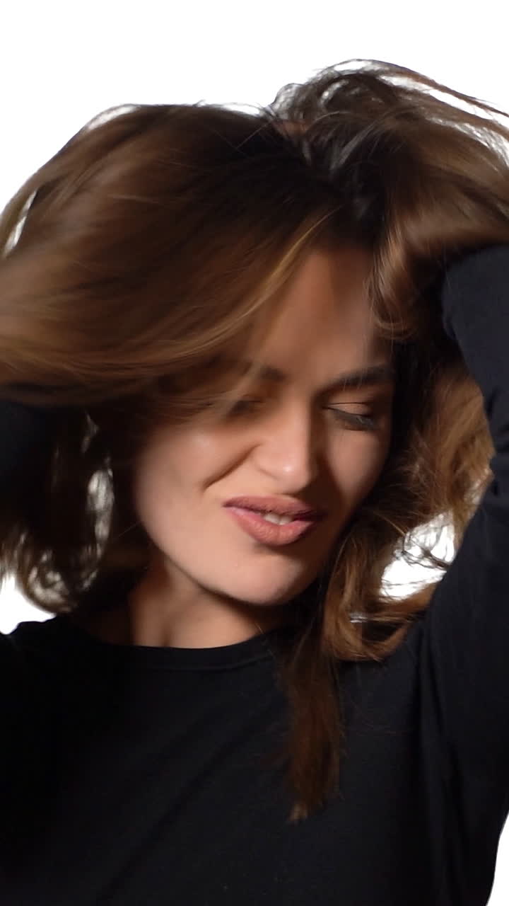 Happy brunette moves her hair and looks at camera. Attractive young girl on white background. Shaking her hair. Slow motion. Vertical video