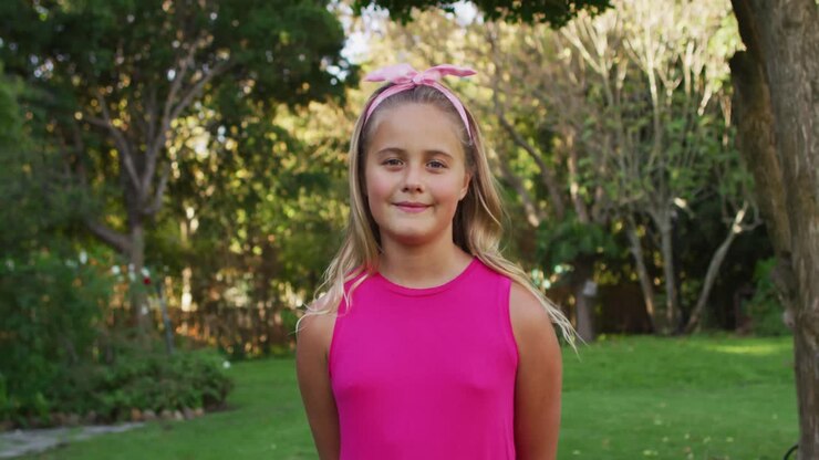 Retrato de niña caucásica feliz de pie en el jardín sonriendo a la cámara