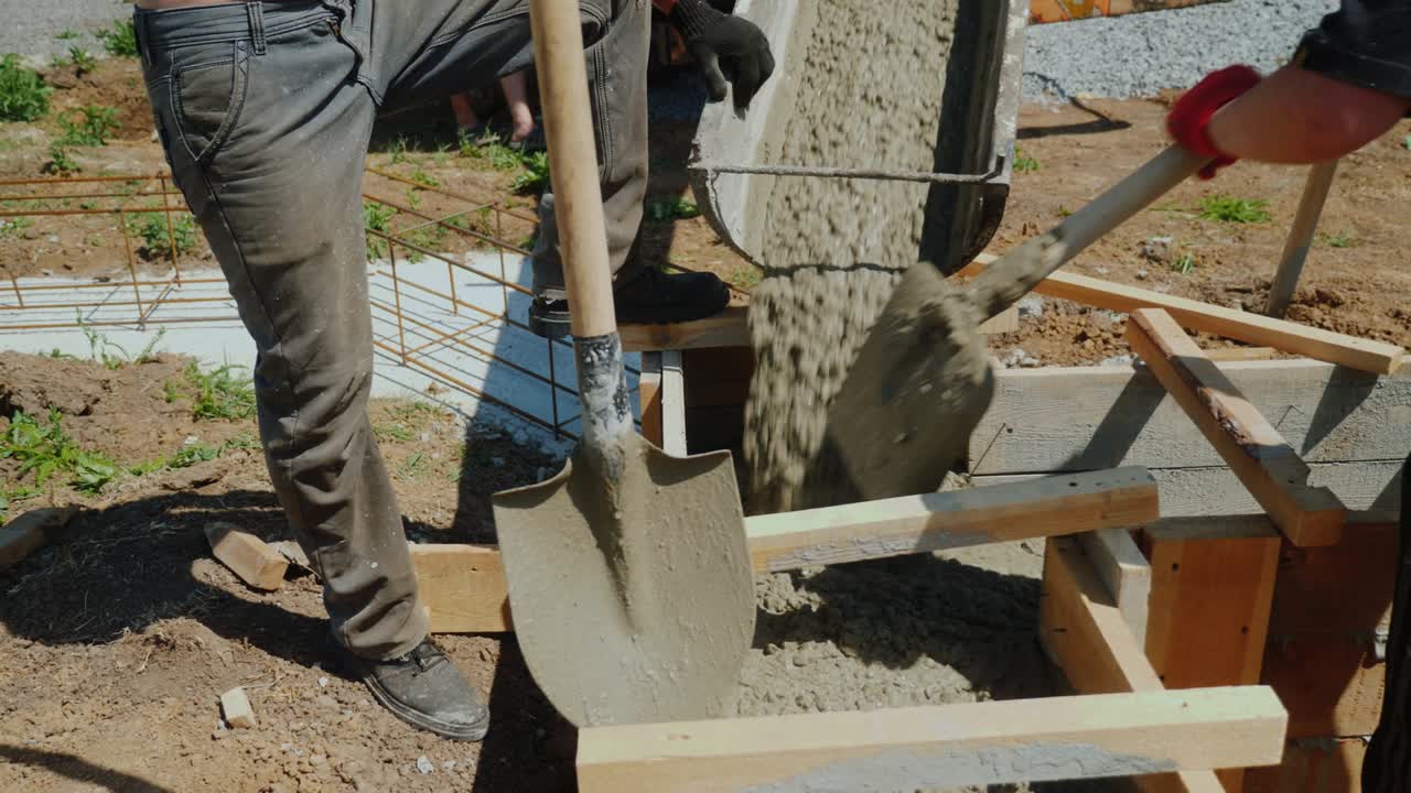 vertiendo hormigón en un molde de madera. cerca hay un trabajador con una pala. construcción de cabañas