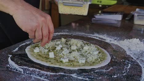 chef añadiendo cubiertas de queso mozzarella triturado a la pizza en la cocina al aire libre rústica