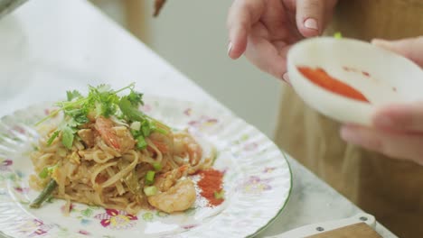 woman adding ground red pepper to wok noodles