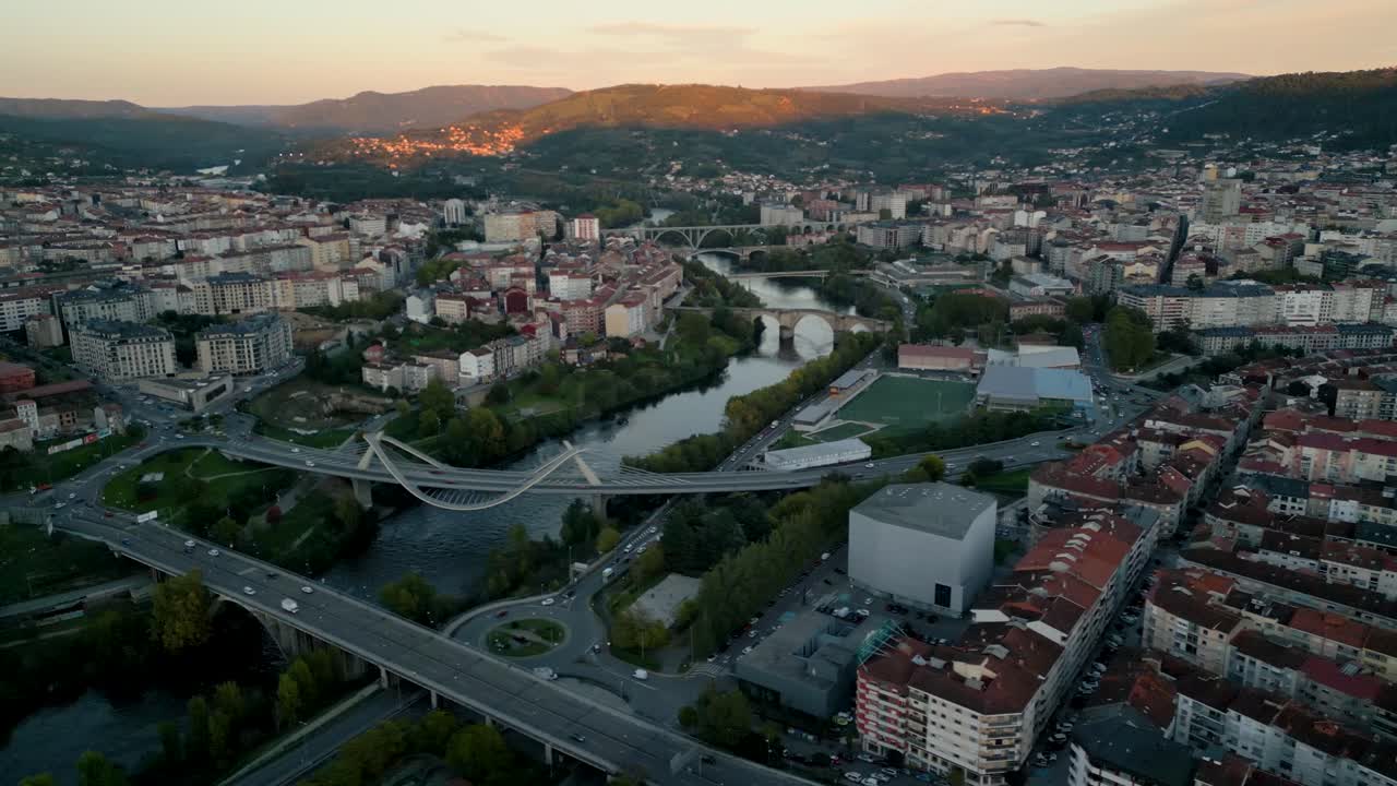 Aerial view of Ourense, Spain at dusk, capturing the cityscape, rooftops, and river illuminated by golden hour light