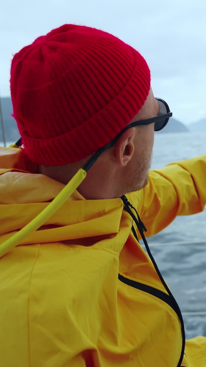 Mann im gelben Regenmantel und roter Mütze segelt auf dem Meer