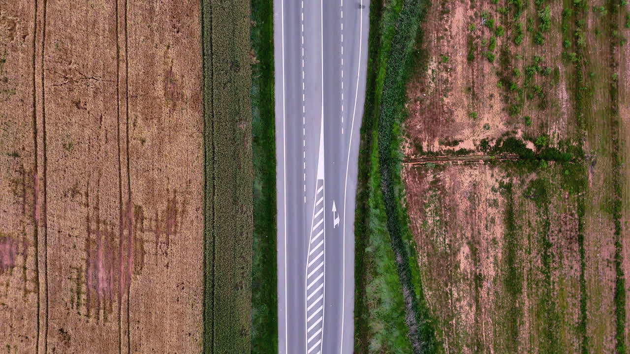 Top-down view of road in La Rioja with clear lane markings. Farmlands with geometric patterns and textures visible on both sides of the road. Minimalist, modern transportation scene