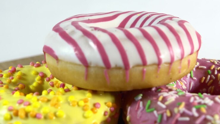 Rotating donuts with different fillings on the table. Delicious sweet donut rotating on a plate. Bright and colorful donut close-up macro shot spinning on a white background. Seamless loop.