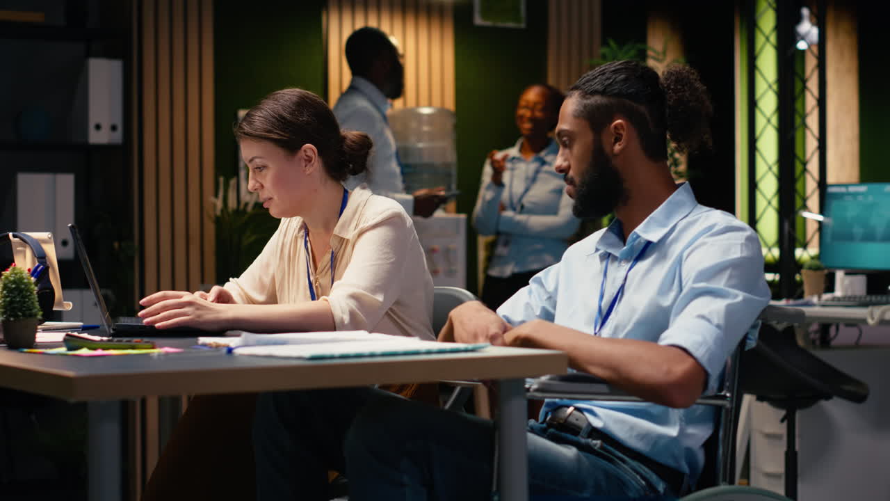 Man wheelchair user and female manager, together in busy corporate office