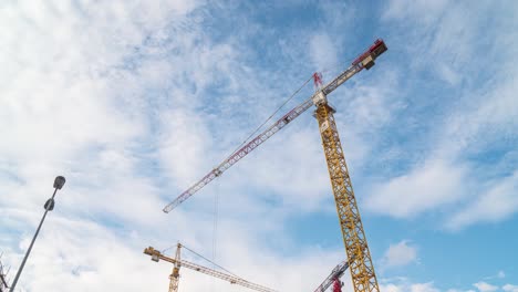 timelapse of cranes on construction site, blue sky with moving clouds, low angle static view