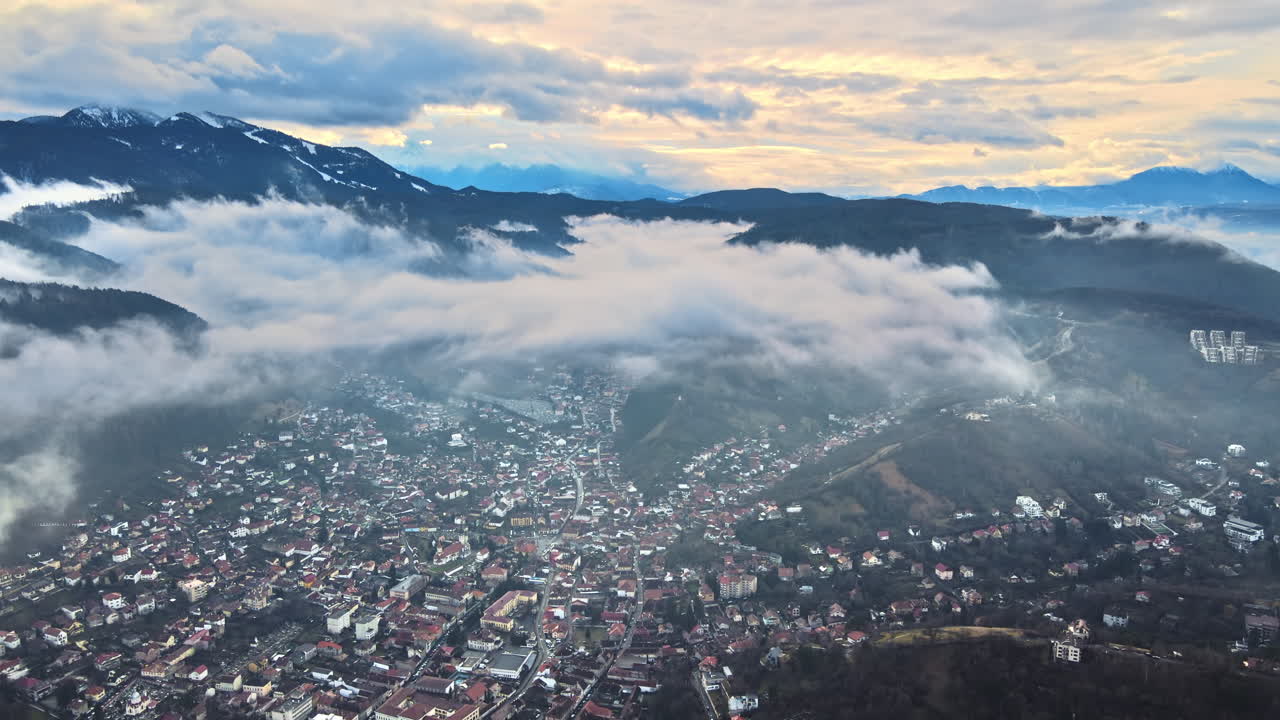 Aerial drone view of Brasov in winter, Romania. Residential buildings, mountains, low clouds and fog in the air
