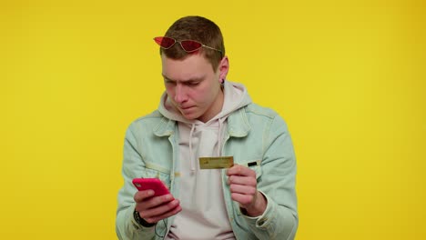 Teen-man-using-credit-bank-card-and-smartphone-while-transferring-money,-purchases-online-shopping