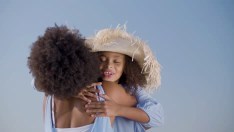 happy girl in straw hat running to her mum, hugging and kissing her at the beach