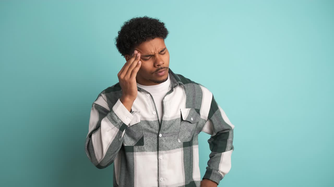 Frustrated man suffering from headache in blue studio