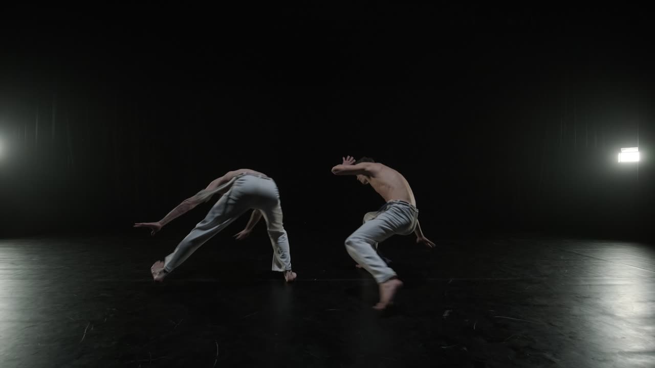 Gruppo di ballerini professionisti che praticano capoeira nell'oscurità contro un riflettore su uno sfondo nero dello studio. Arte marziale afro-brasiliana che combina elementi di danza