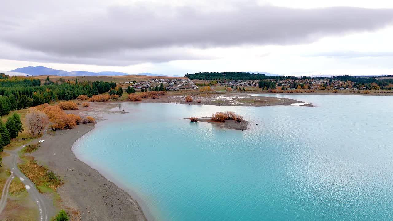 Aerial footage captures Lake Tekapo's turquoise waters and surrounding landscape under overcast skies, creating a peaceful and serene atmosphere