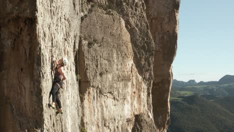 Mujer-Escalando-En-Una-Pared-De-Acantilado-De-Montaña-Muy-Empinada-Durante-El-Verano---Escalada-En-Roca-Al-Aire-Libre---Toma-Aérea-De-Drones