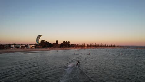 Dron-Siguiendo-A-Un-Surfista-De-Cometas-Desde-Atrás-En-Un-Océano-Plano-Mientras-Se-Ponen-Las-Puestas-De-Sol