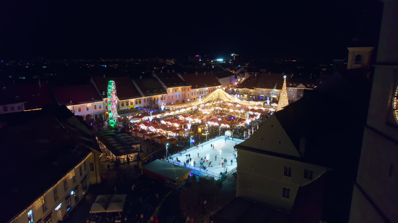 View of the Historic Centre of Sibiu with Christmas fair, Romania. The Great Square decorated with ferris wheel, Christmas tree, ice rink, illumination, old buildings and multiple people