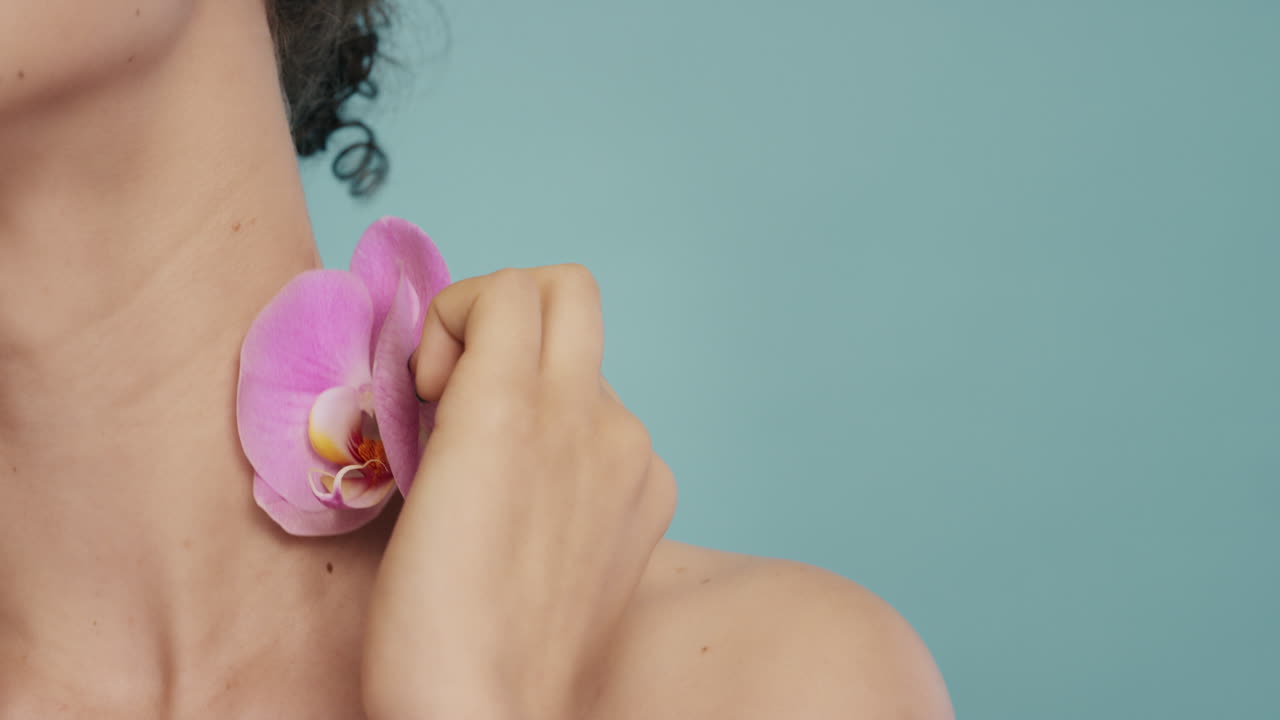 ritratto di bellezza da vicino donna che tocca il corpo con un colorato fiore d'orchidea rosa che accarezza una pelle liscia e sana che gode di una fresca fragranza naturale concetto di cura della pelle