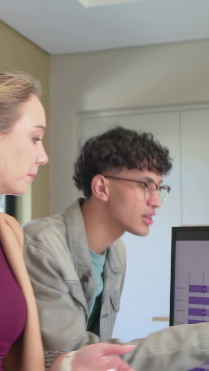 Video verticale: Donna con blazer color cuoio che entra nella stanza, indicando lo schermo mentre un uomo si unisce per modificare un grafico tramite laptop.