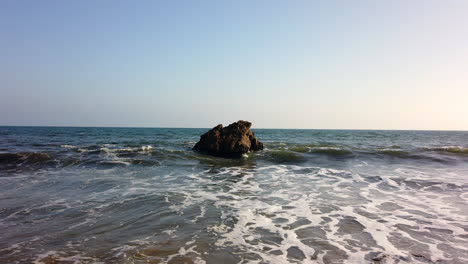 a rock on the beach of malibu with water flowing around it