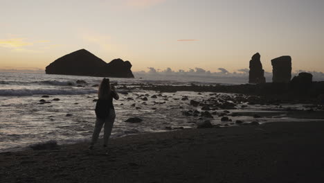 Woman-takes-pictures-of-rocky-horizon-from-Azores-beach,-wide-handheld