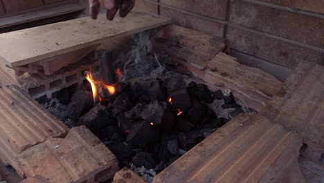 slow motion wide shot of man placing charcoal briquettes onto a lit charcoal greek style bbq