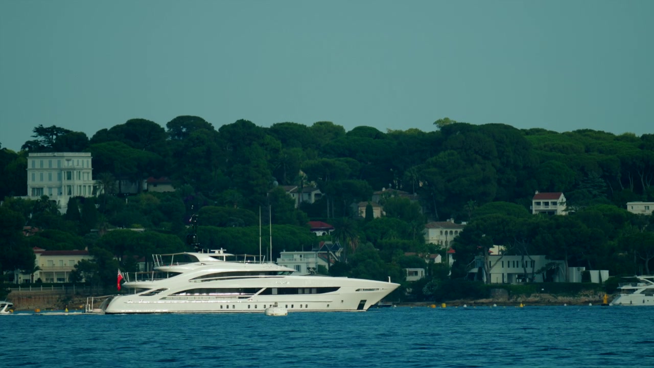 Superyacht di lusso bianco che naviga nelle calme acque del Mar Mediterraneo con ville e le verdi colline di Cap d'Antibes visibili sullo sfondo, Antibes, Francia