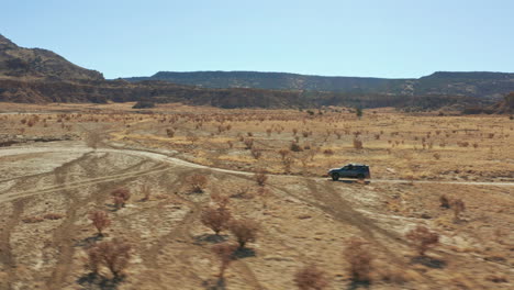 tracking aerial following fast moving car racing down desert dirt road, 4k