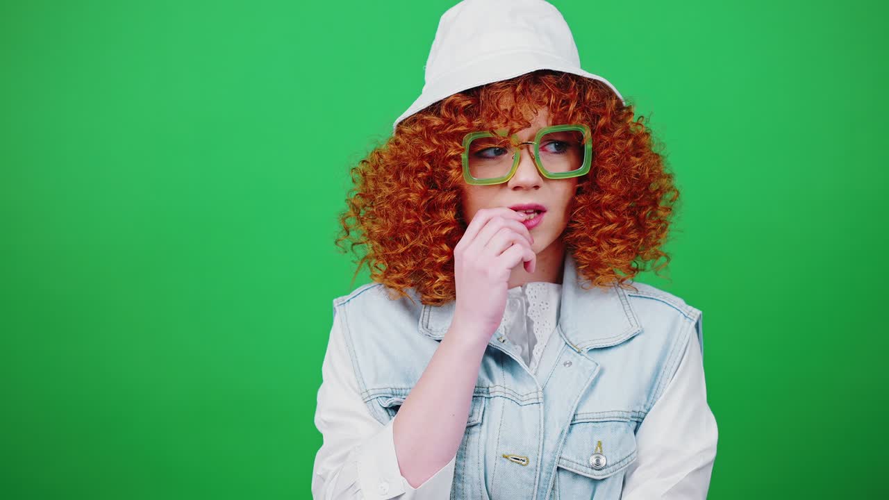 안경과 파나마 모자를 입은 젊은 긴장한 은 머리 여성이 손가락을 고, 크로마 키 배경에 자신을 포옹합니다.
