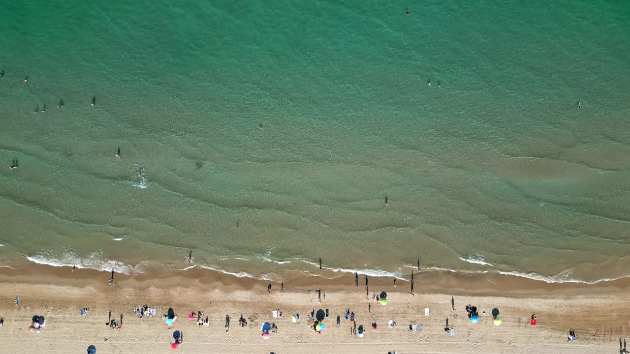 Aerial drone view of people relaxing on the beach with hitting the shore in Alicante, Spain