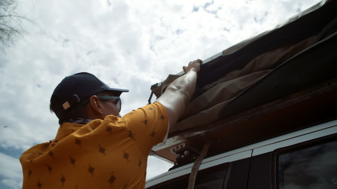 Hand held shot of a off-roading Caucasian male tourist in Africa walking towards a folded up rooftop tent and tucking it in