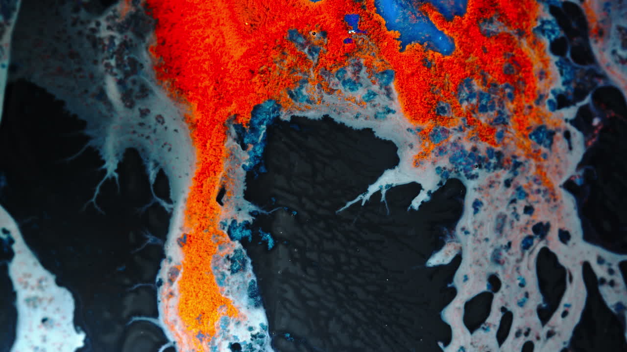 Abstract ink macro shot with vibrant reds, blues, and whites blending on black surface