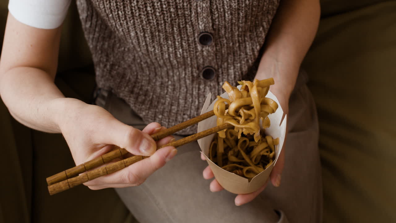 Close-up of a person eating noodles with chopsticks from a takeout box
