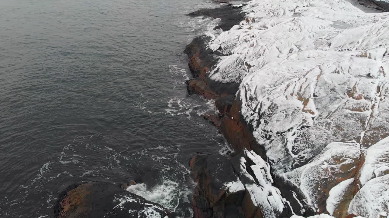Aerial of coastline with snow on rocks and waves. In Norway 4K