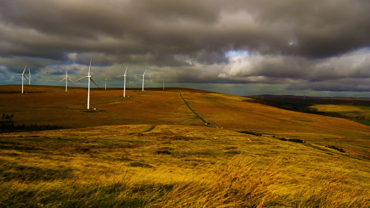 Timelapse with Dark Clouds Moving Over Renewable Energy Wind Farm with Propellers Spinning Rapidly Creating Green Energy Electricity. Industrial Natural Landscape in Wales, UK