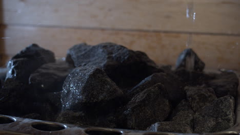 Water-pouring-over-steamy-rocks-in-Finnish-sauna,-close-up-shot