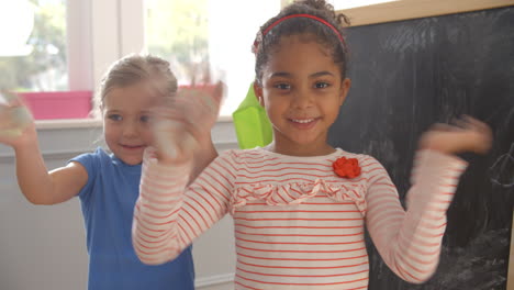 Two-Girls-By-Blackboard-Waving-At-Camera