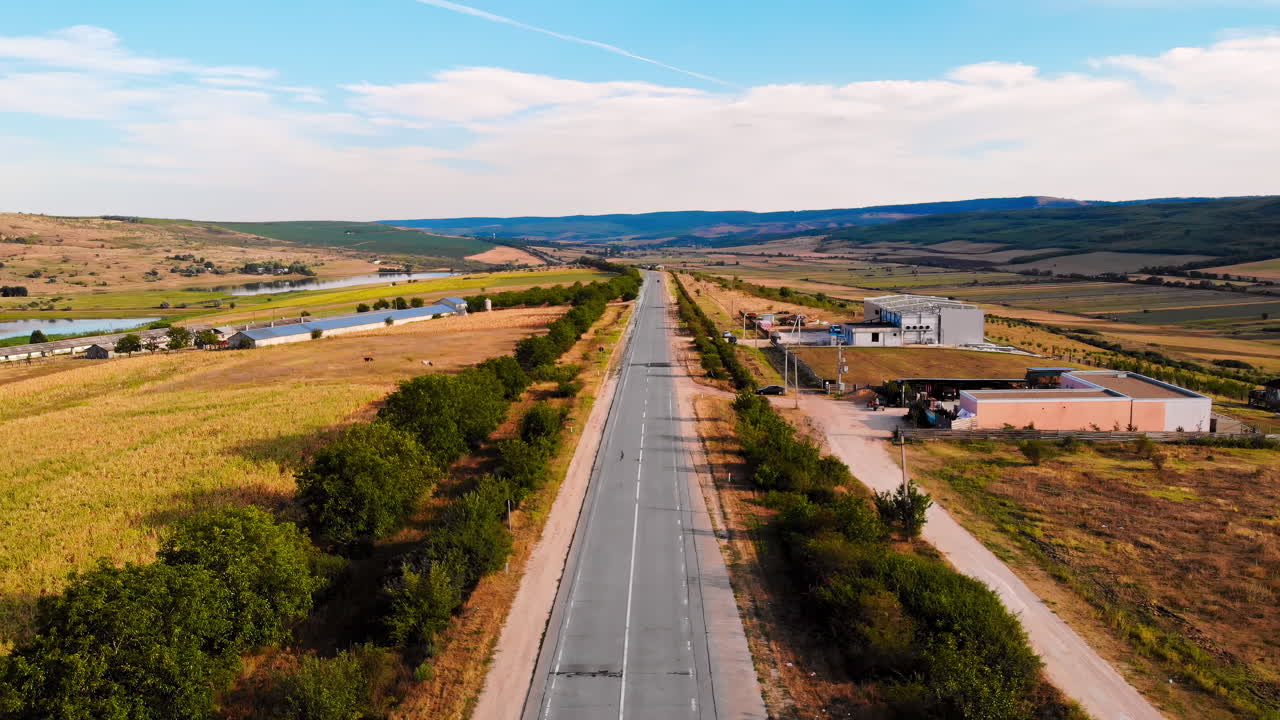 Aerial drone view of a road without moving cars in highland. Small village and green hills on background. Sunny day. Balti, Moldova