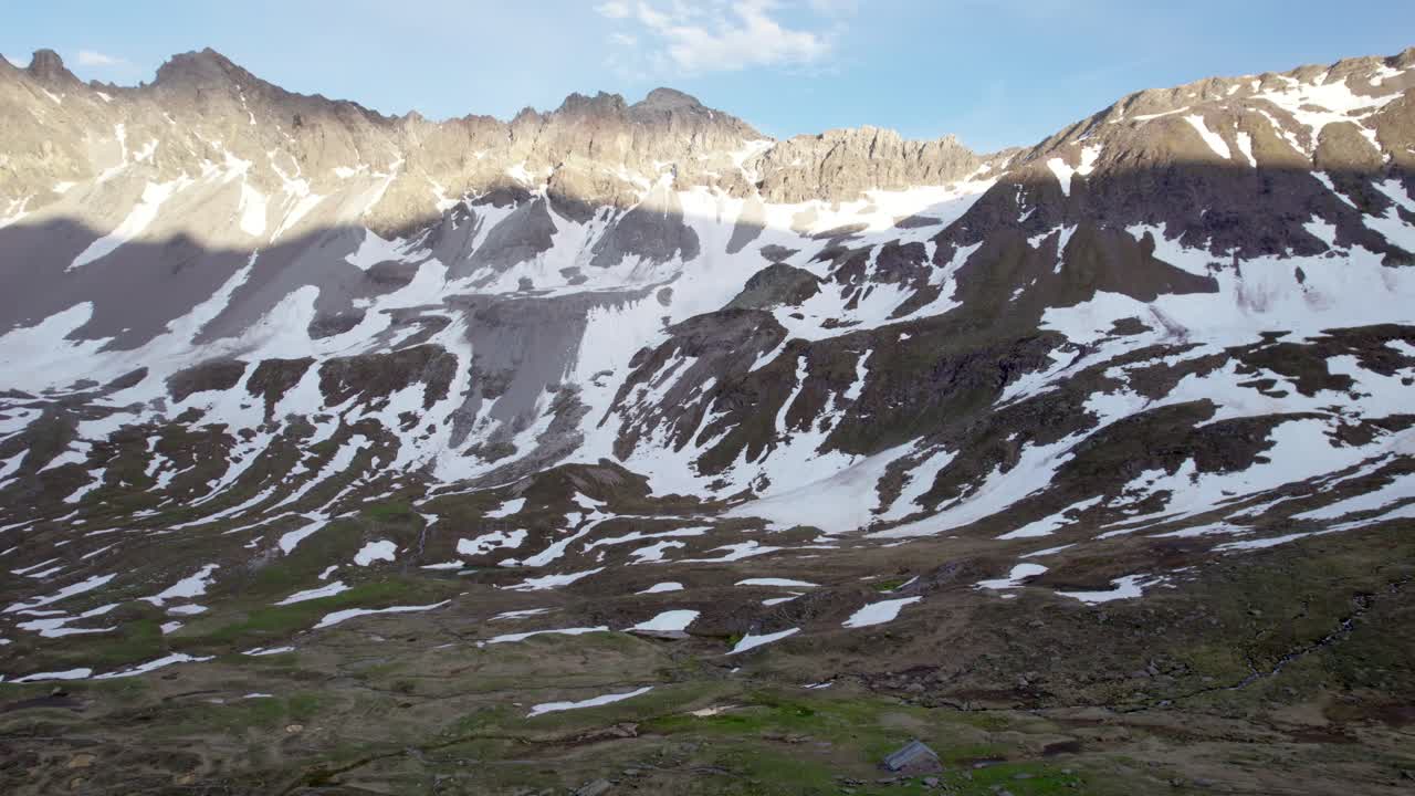 imágenes de drones aéreos girando lentamente hacia arriba a través de un espectacular paisaje montañoso irregular con parches residuales de nieve y prados alpinos para finalmente revelar un valle glacial en suiza