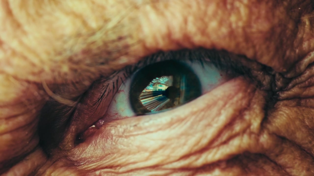 Macro close up of an older person's eye with fast, jerky, unsettling movements, creating a demonic and evil stare. Intense horror concept of a scary creature or monstrous presence looking at you. 4k.