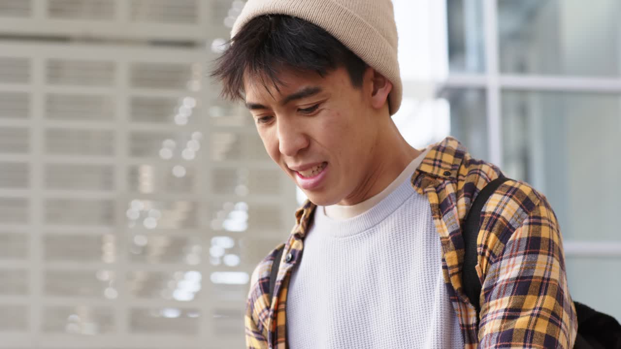 駅でスマートフォンをタップし、スマートウォッチを確認し、頬を膨らませて待っている20代のアジア人男性。