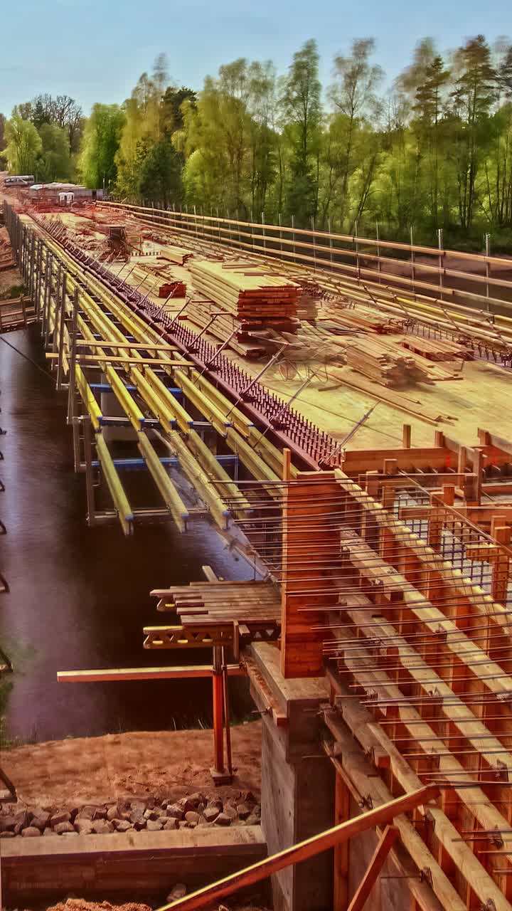 A time-lapse of work progress on a new bridge construction site, with formwork and rebar being installed on steel girders spanning a wide river in Latvia