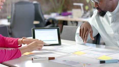 Diverse-colleagues-discussing-work-with-documents-on-table-and-tablet-in-office-in-slow-motion