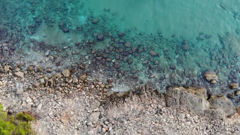 Schöne-Luftaufnahme-Der-Klippe-Mit-Dem-Meer,-Ein-Klares-Blaues-Und-Türkisfarbenes-Meer-Mit-Kristallklarem-Und-Ruhigem-Wasser-Lässt-Sie-Die-Felsen-Im-Hintergrund-Auf-Einer-Reise-Von-Links-Nach-Rechts-Sehen