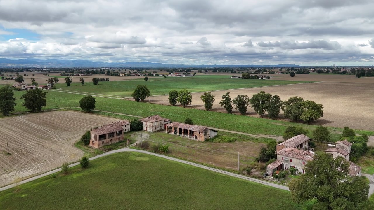 Terreni agricoli della Pianura Padana vicino alla confluenza dei fiumi Trebbia e Po in provincia di Piacenza, Emilia-Romagna, Italia, con coltivazioni di cereali, cascine rurali e le colline pedemontane dell'Appennino settentrionale, sorvolo aereo.