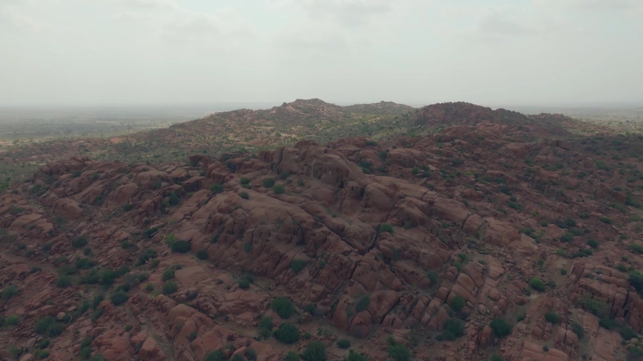 Ampio panorama drone su colline di granito rossastro nel deserto del Thar, Sindh, Pakistan, con creste arrotondate che digradano verso pianure sabbiose e brumose con rada vegetazione