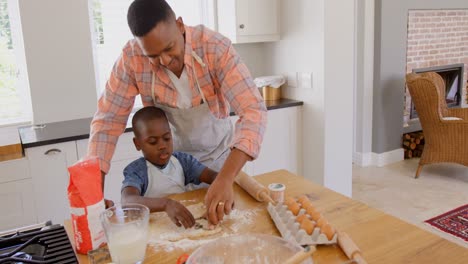 Front-view-of-mid-adult-black-father-and-son-baking-cookies-in-kitchen-of-comfortable-home-4k