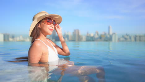 Seitenansicht-Einer-Wunderschönen-Thailändischen-Frau,-Die-Sich-In-Einem-Swimmingpool-Auf-Dem-Dach-In-Bangkok-Mit-Panoramablick-Auf-Die-Skyline-Der-Stadt-Entspannt