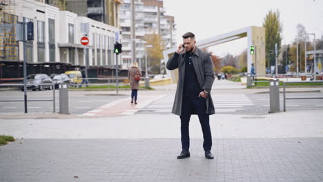portrait of a handsome young businessman dressed in formal clothes. male in coat crosses the road and using mobile phone.